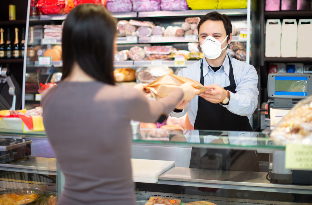 Smiling shopkeeper serving a customer while wearing a mask, coronavirus pandemic concept 