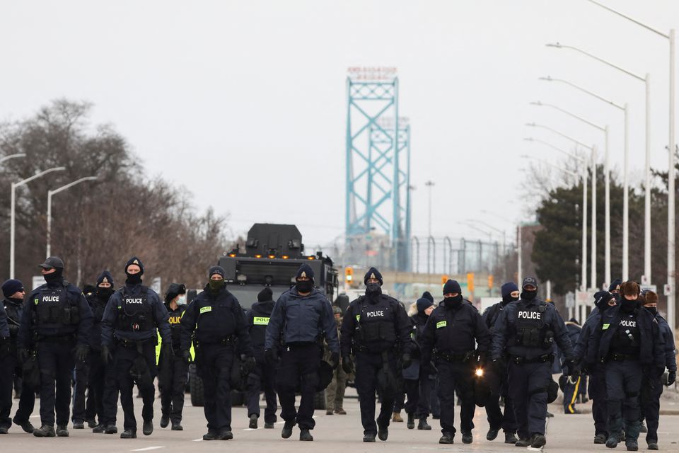 Police officers move along a road leading to the Ambassador Bridge, which connects Detroit and Windsor, after clearing demonstrators, during a protest against coronavirus disease 